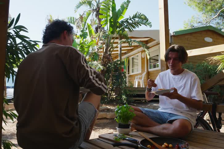 Two male friends sitting on wood deck eating spaghetti