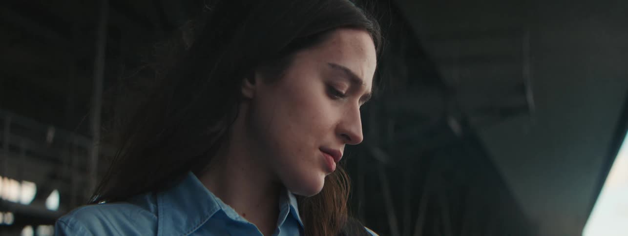 A woman stands outside looking off into the distance and then looking down