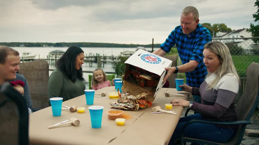 Family sitting at a table and a smiling man dumping a box of crabs