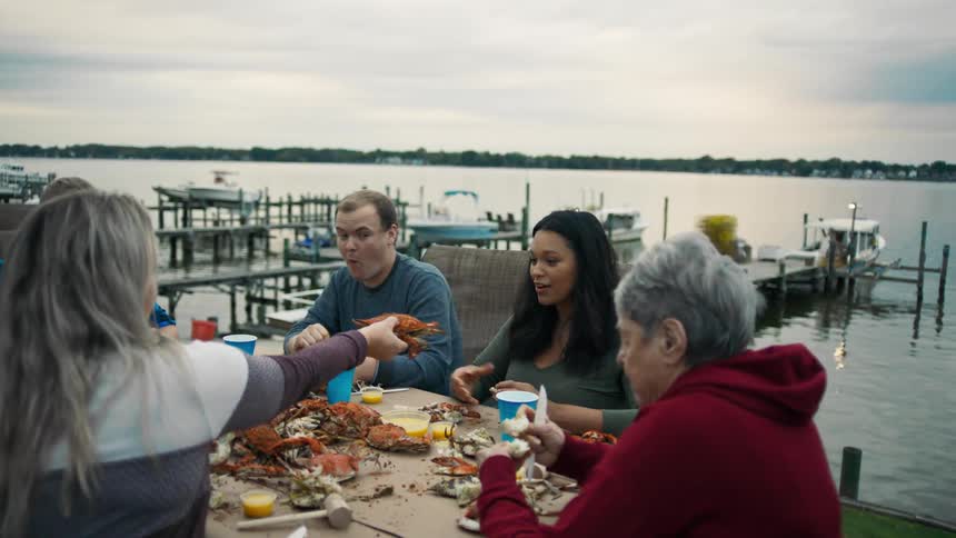 Group of people including men and women sitting at a table by the sea eating crab