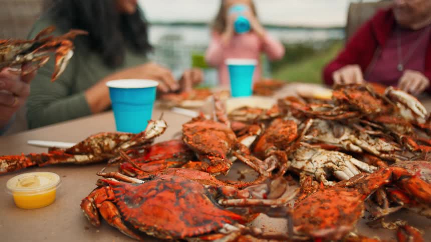 Person picking up a cooked crab from a pile on the table