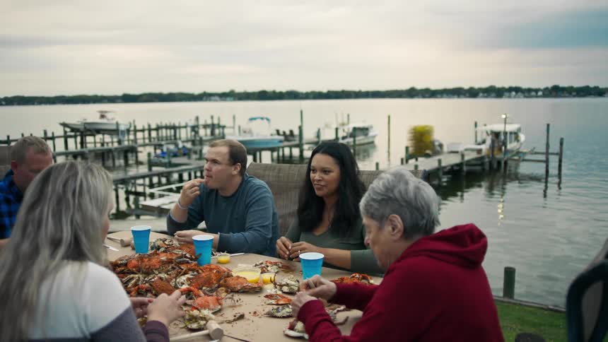 Family sitting at an outdoor table on the edge of the pier eating crab