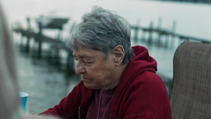 An elderly woman sitting in a chair on the edge of a pier