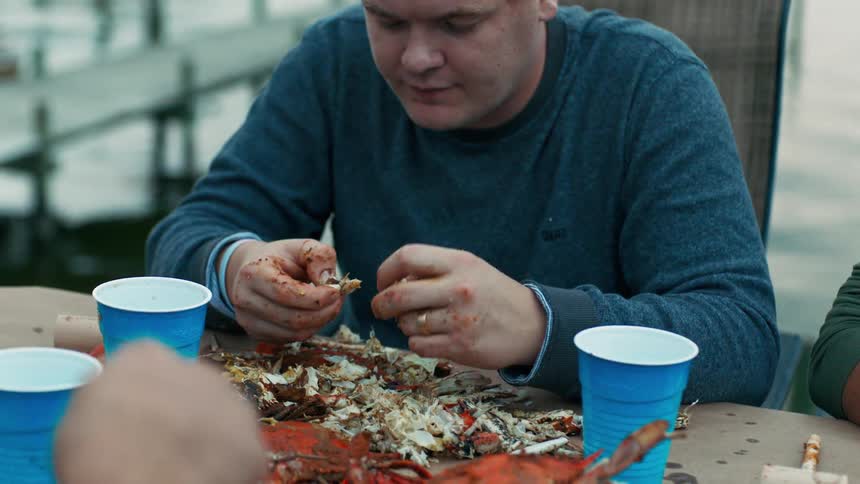 A man in a blue shirt is on a pier peeling a seafood