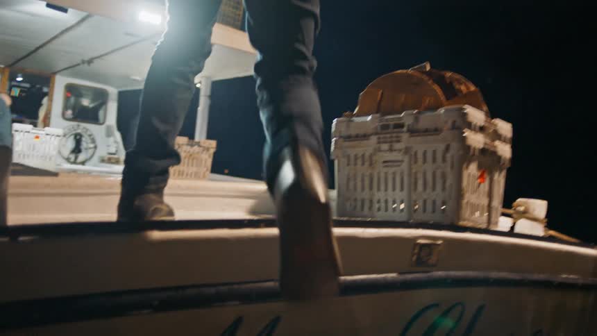 Legs of a man entering a fishing boat at night moored in a port