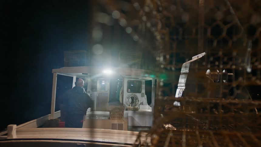 A man stacks crates onto a fishing boat at night
