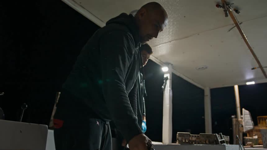 Man with a water hose cleaning and running his boat at night