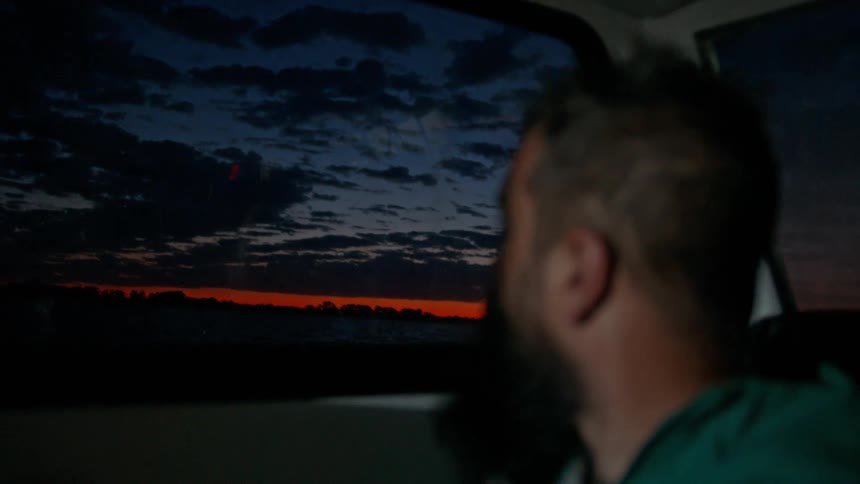 A man on a boat watching the red sky before dawn