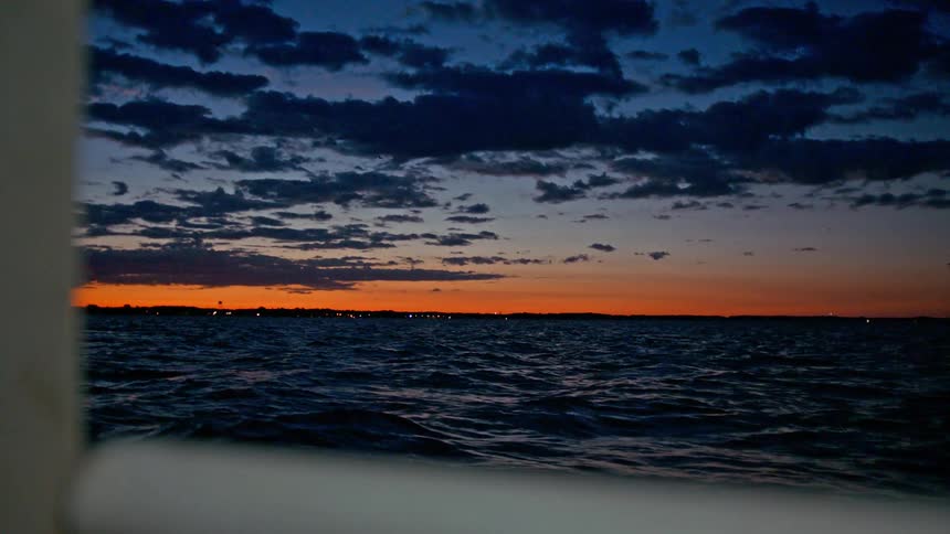 A view of the sunset at the edge of the ocean from a boat
