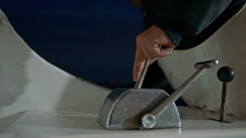 A hand pulling levers on a boat at night