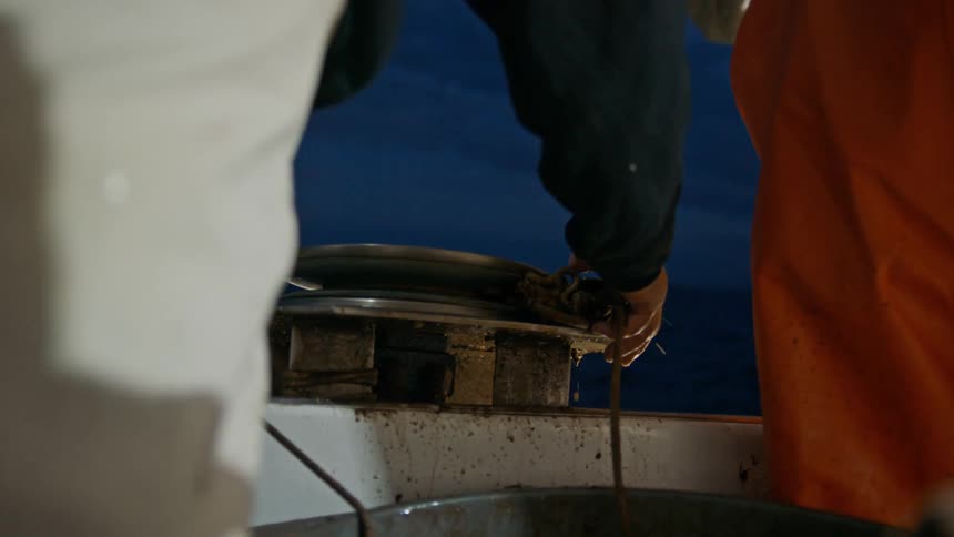 One man holds a rope passing over a pulley while the other holds a metal cage