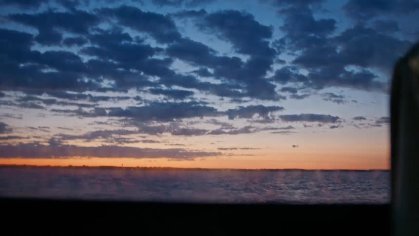 View from the window of a boat moving through the sea with the purple and reddish sky on the horizon