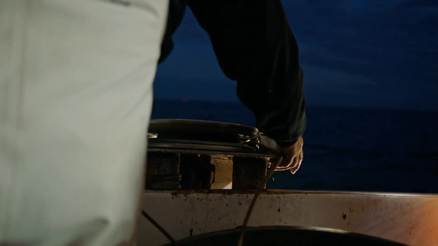 Hands of a man releasing a rope from a valve on a boat in the middle of the sea at night