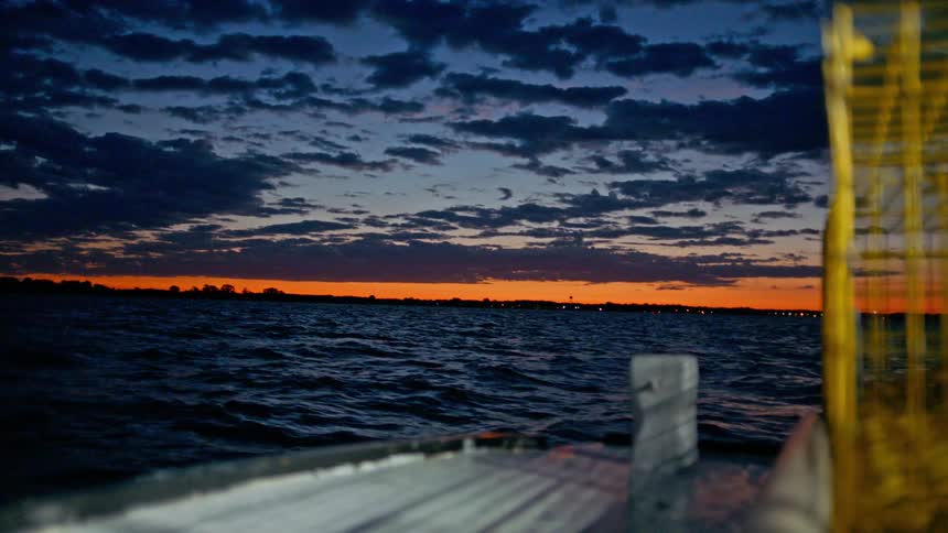 Small fishing boat moving through the sea with orange sky on the horizon at dusk