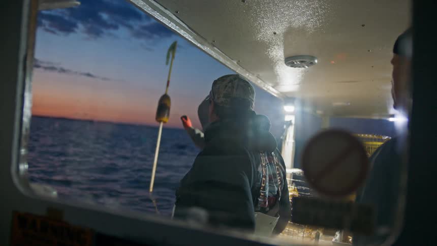 Three men inside a fishing boat moving through the sea on a late afternoon with a red sky