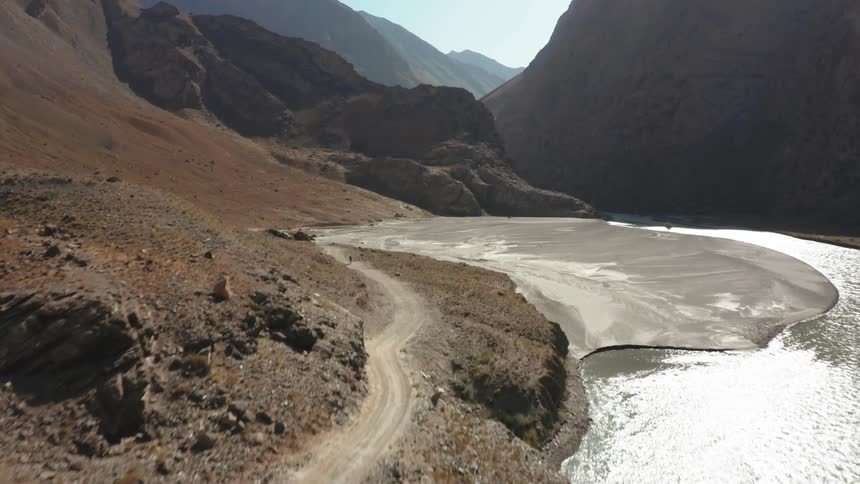 Joggers run along the dirt road between mountains and the water
