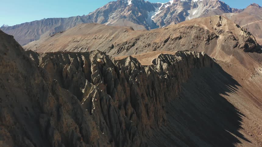 A long mountain edge is lined with a jagged cliff in this arid landscape