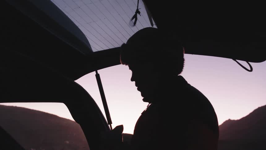 Silhouette of a man removing socks from his boots placing them in the back of his vehicle