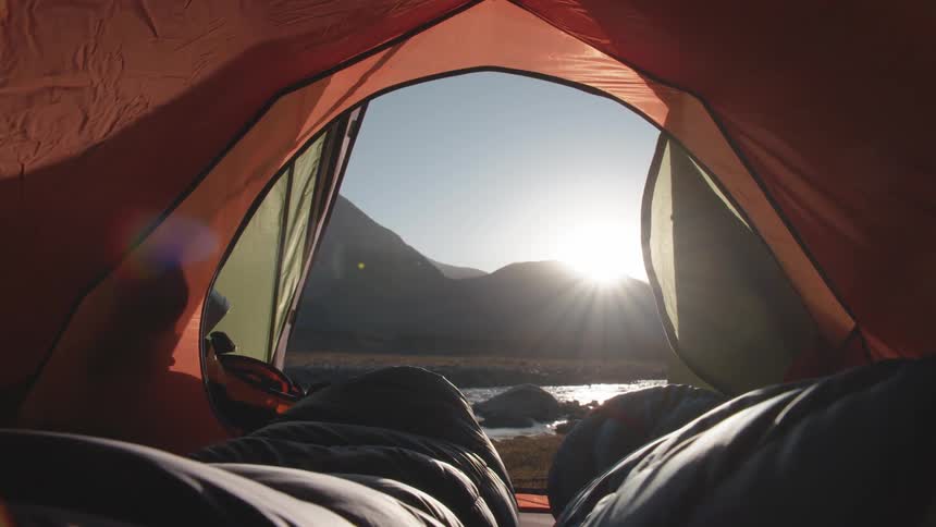 Camping by a river at sunrise inside tent