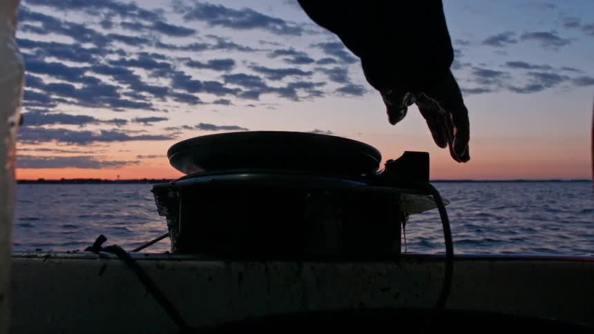 Hands of a man guiding the rope of a boat moving across the sea in the reddish morning sky