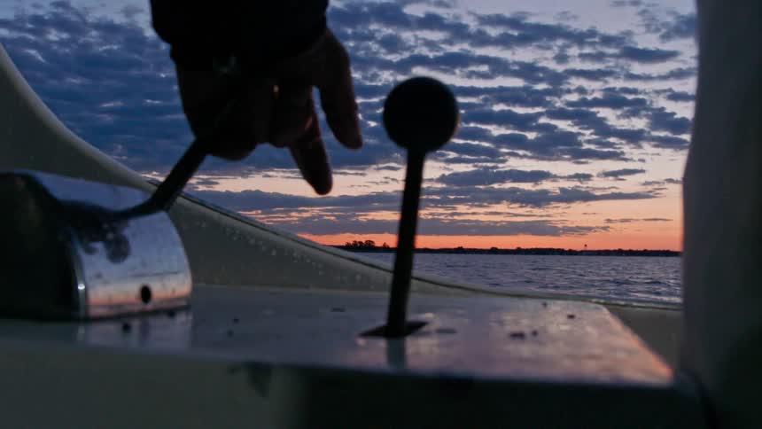 A person moving levers on a boat in the middle of the ocean during sunset