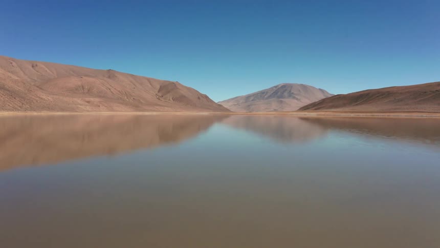 Panorama of a reflective lake with rocky mountains around on a cloudless blue sky day