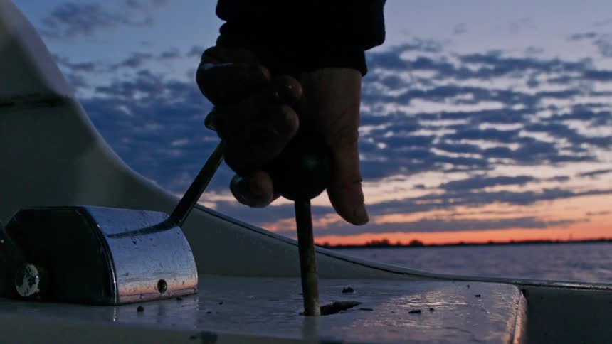 Hands of a man working the crank of a boat at sea on a late afternoon with a red sky