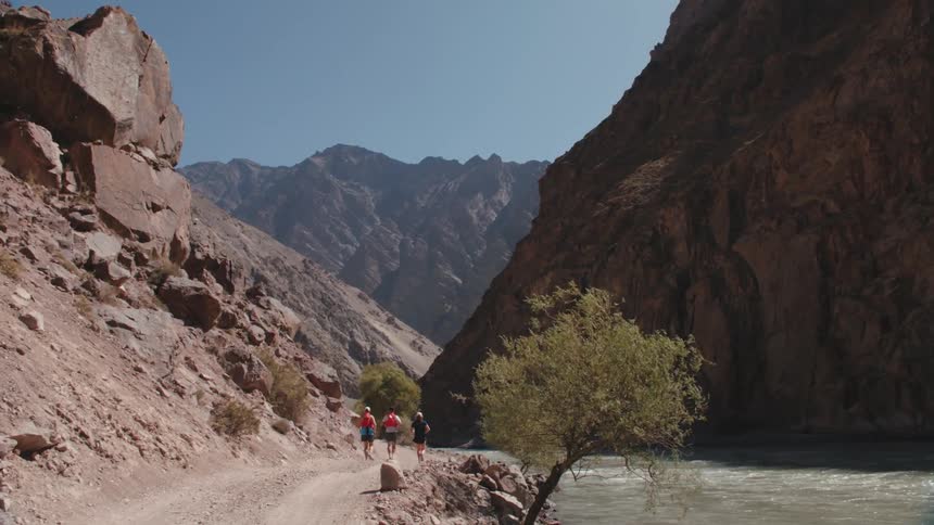 Three people jogging on a dirt road next to a river