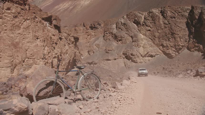 Bicycle parked along dirt road as cars drive by through the desert valley