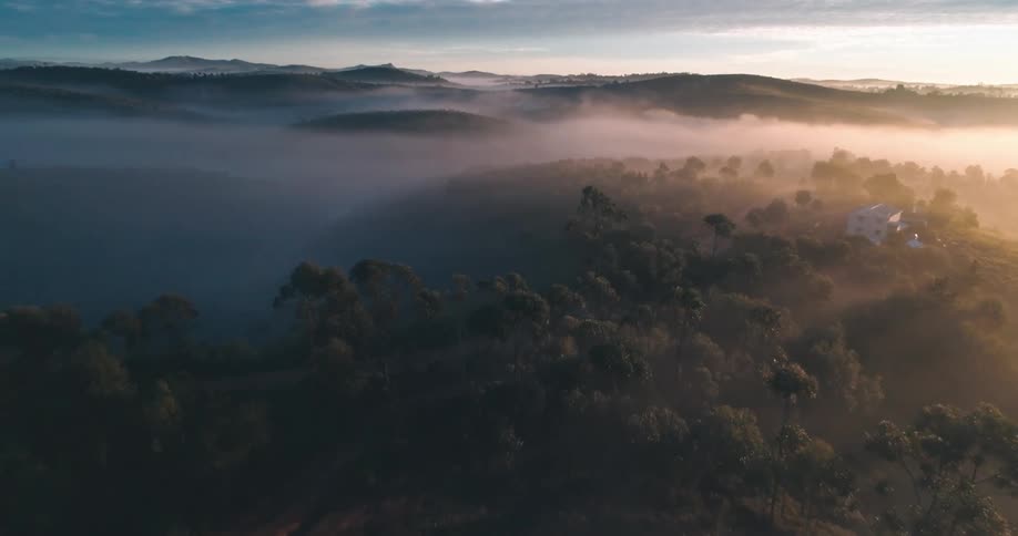 Aerial panorama of an isolated house on the peak of a mountain in the middle of forests on a foggy morning
