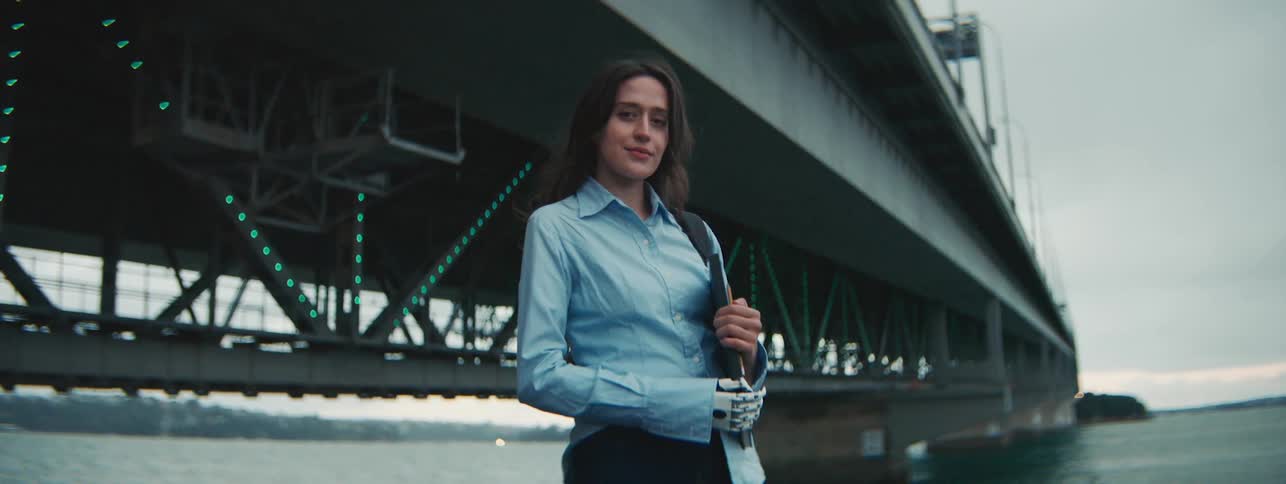 Young woman with robotic arm on the edge of a bridge and the sea giving a smile