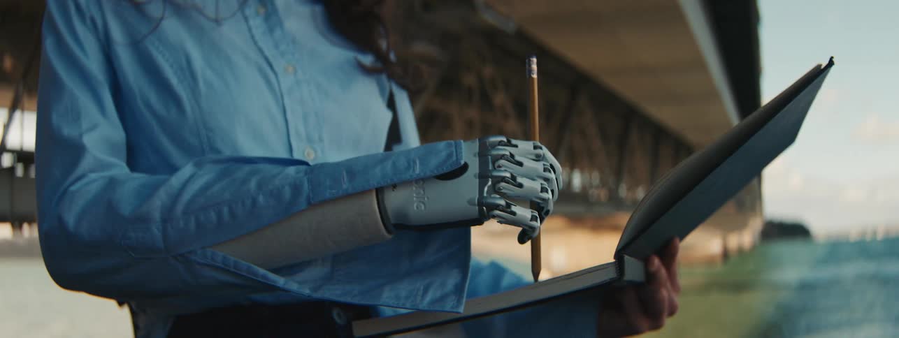 A woman with a robotic arm draws in a pad