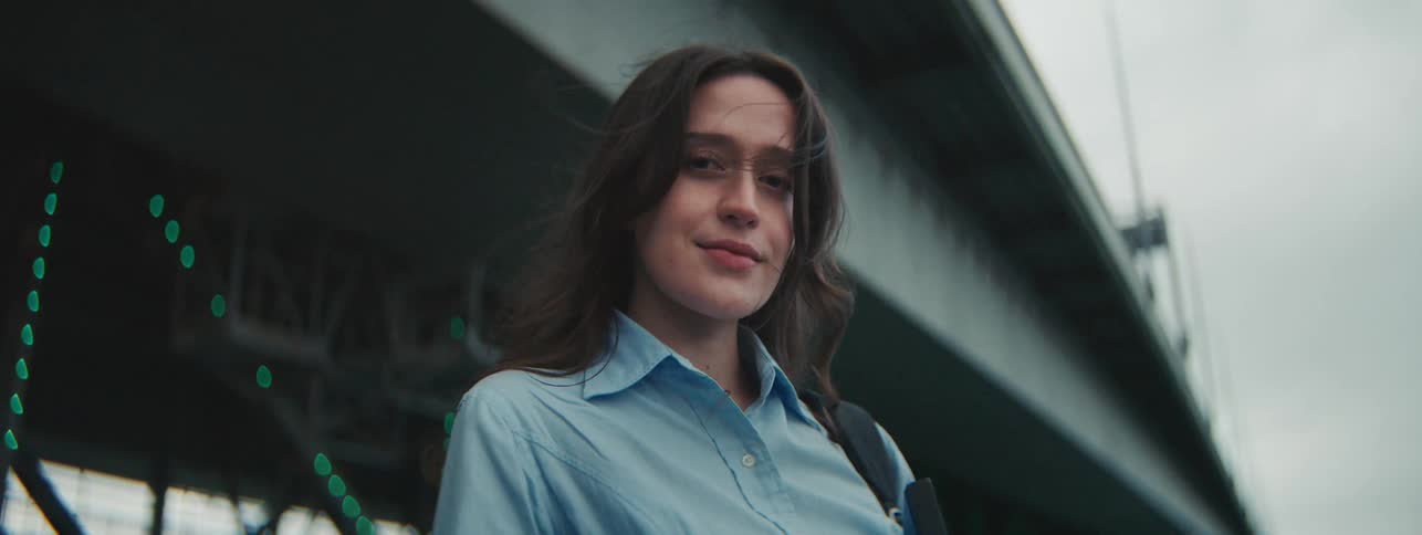 A woman stands outside near a bridge