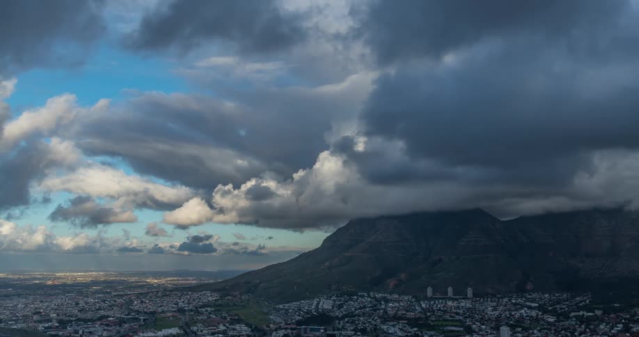 Time lapse of clouds moving over a city next to the mountains