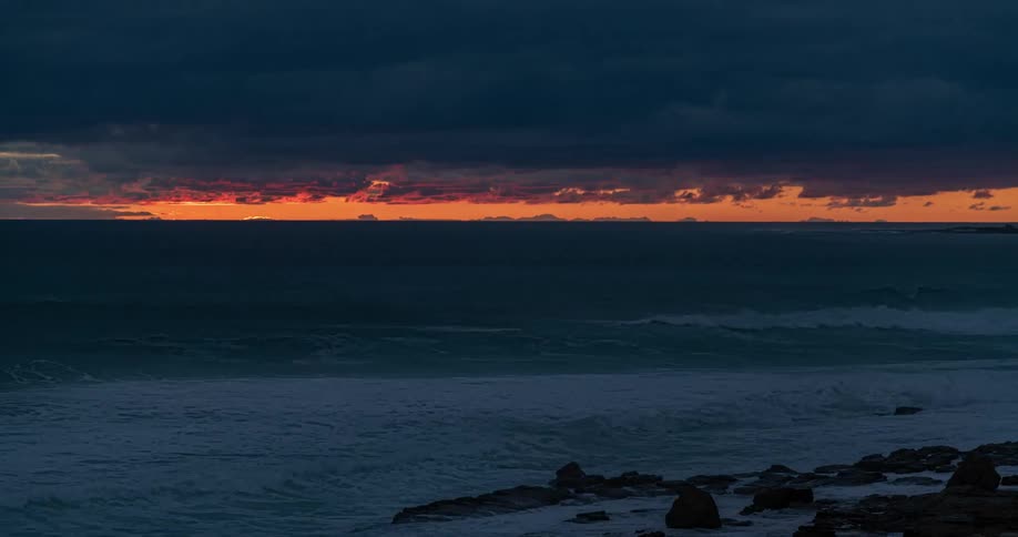 Waves roll onto the rocky shore as the sun sets
