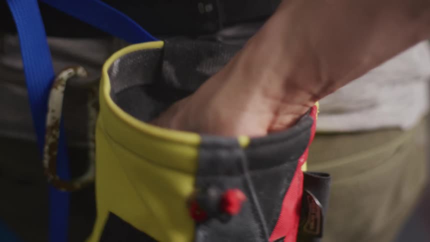 A person reaches their hand into a chalk bag used for climbing