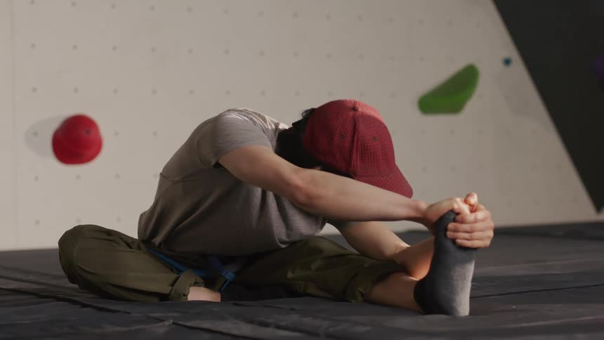A young man stretches on the mat in front of an indoor climbing wall