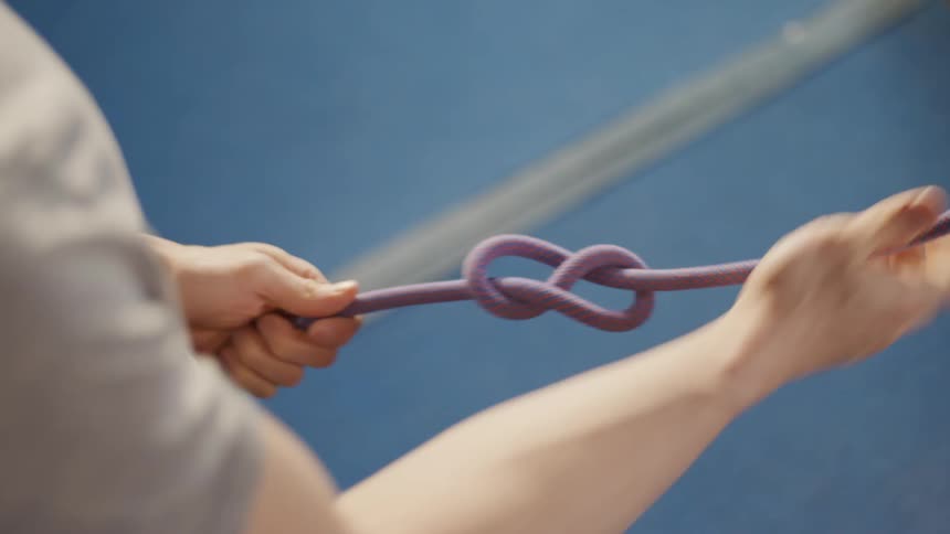 A man tying knots on a thick rope then fastening it to his belt