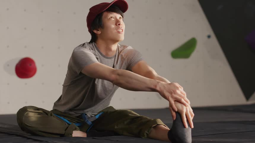 Young man stretches on the floor before climbing a wall