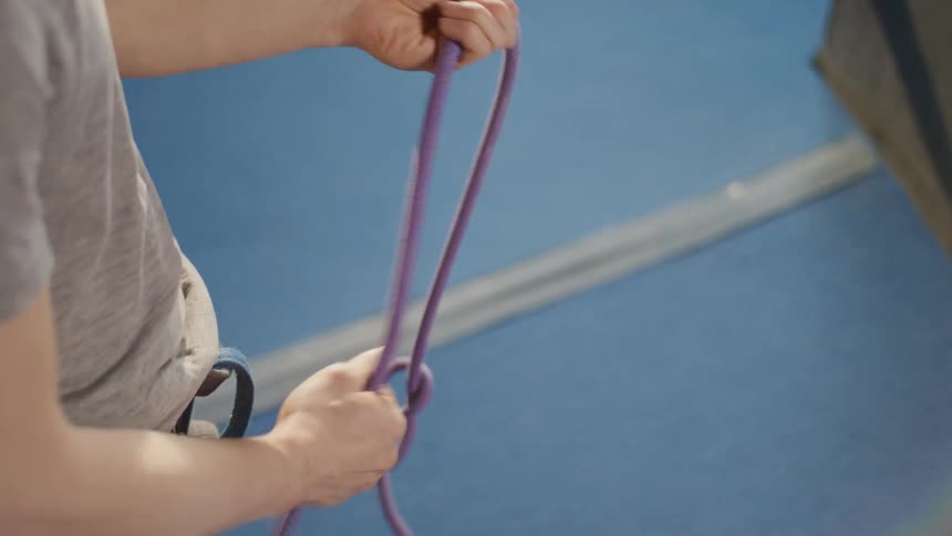 A man tying a red rope to make a knot for his rope climbing harness