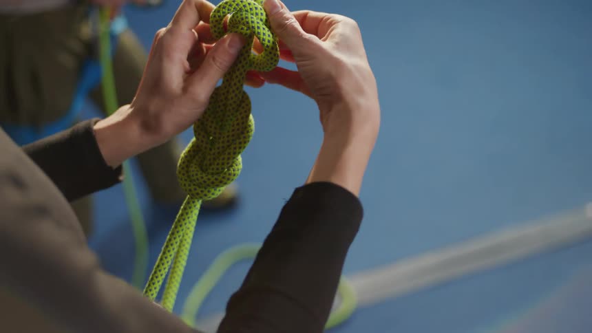 Woman tying a green rope and making two knots for her climbing harness
