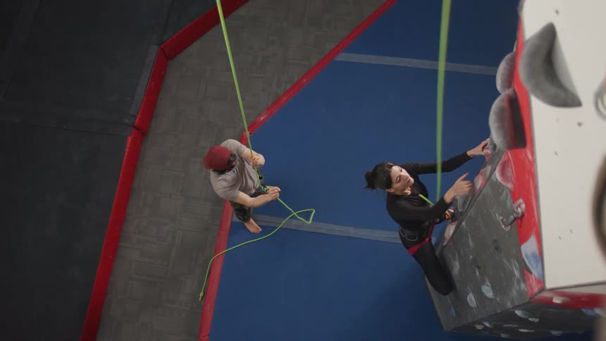 A woman practicing wall climbing while a man pulls and holds her security rope