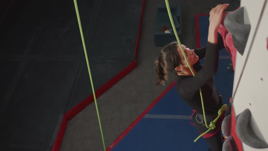 Woman with safety belt climbing a climber training wall