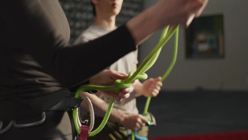 A woman and man are tying ropes to the climbing harnesses attached to their waists