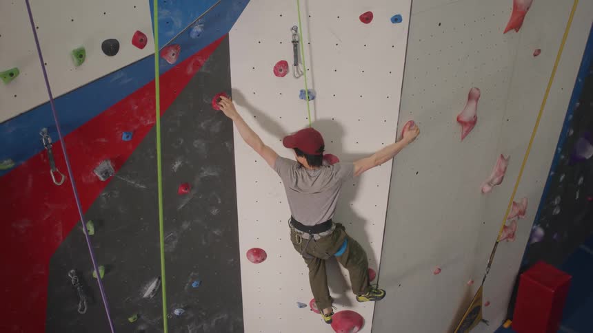 An asian man climbs in a climbing gym