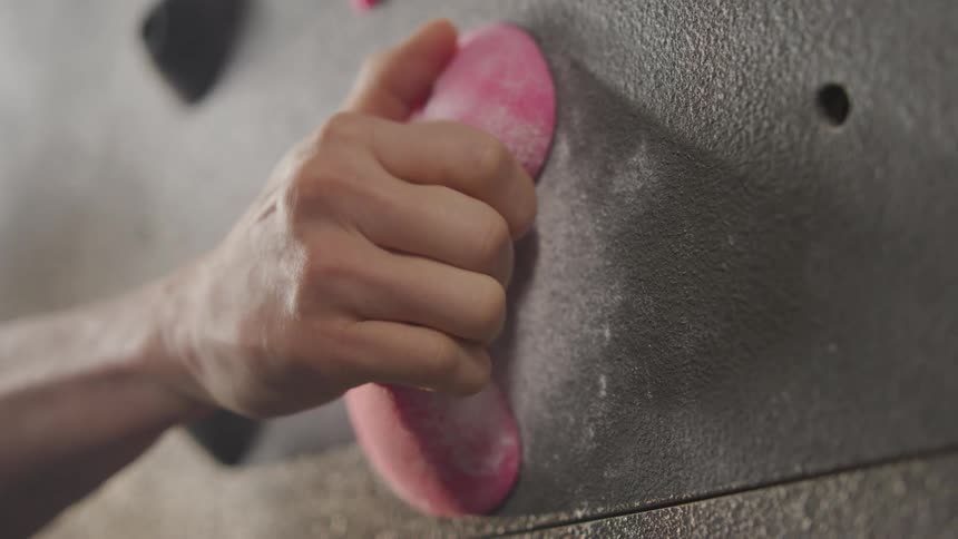 A mans hand gripping a rock hold on a climbing training wall