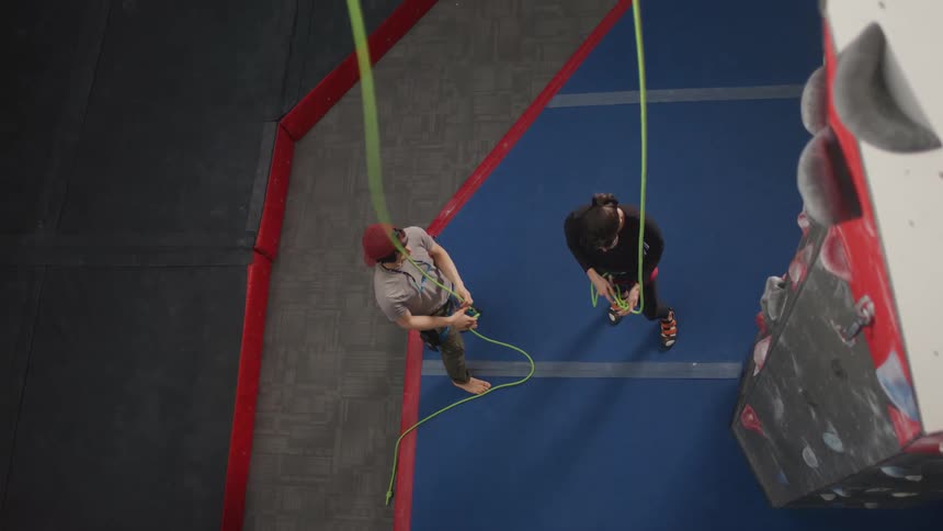 Man and woman next to a mountaineering training wall adjusting the ropes of a safety harness