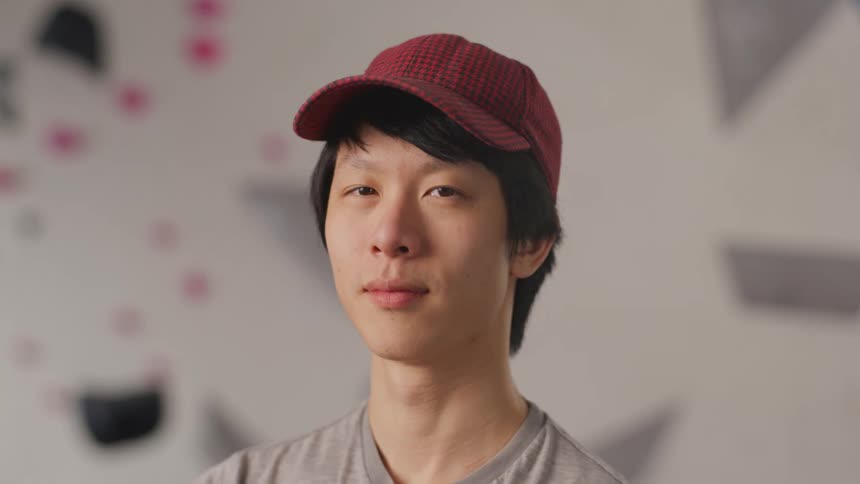 A young asian man wearing a red cap looking to the side and then looking straight ahead
