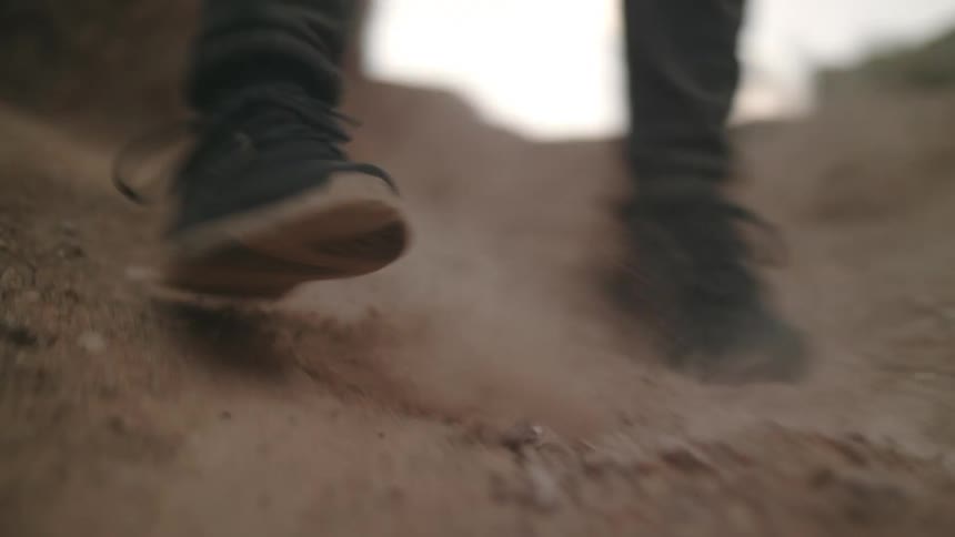 A hiker slipping as he goes down a dirt track on a steep hill