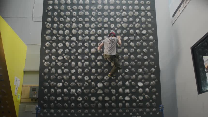 A man scales a kilter board wall in a climbing gym